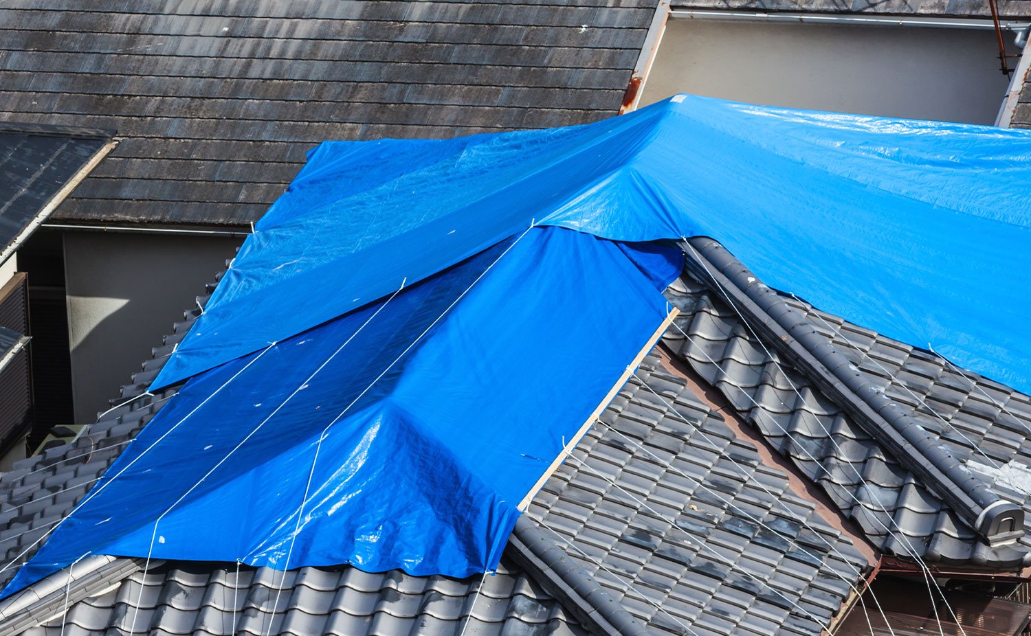 Blue tarp on a building roof in need of emergency roofing repairs to prevent further damage.