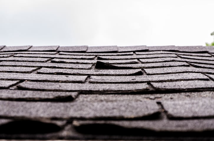 Shingles on a roof with curled corners from wind damage.